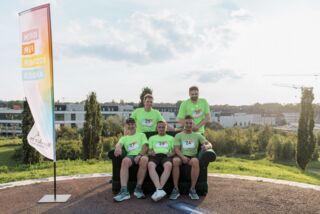 Fünf Männer in grünen Laufshirts sitzen und stehen auf einem Sofa vor dem Förderturm-Firmenlauf – Gruppenfoto mit weitem Ausblick im Hintergrund