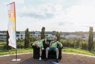 Fünf Männer in grünen Laufshirts sitzen und stehen auf einem Sofa vor dem Förderturm-Firmenlauf – Gruppenfoto mit weitem Ausblick im Hintergrund