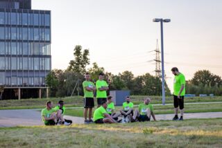 Teilnehmende des Förderturm-Firmenlaufs in grünen Shirts erholen sich nach dem Lauf auf einer Wiese – einige sitzen, andere stehen