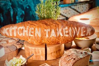 Großer Brotlaib mit dem Schriftzug ‚Kitchen Takeover‘ aufgeschnitten und angerichtet auf einem Buffet