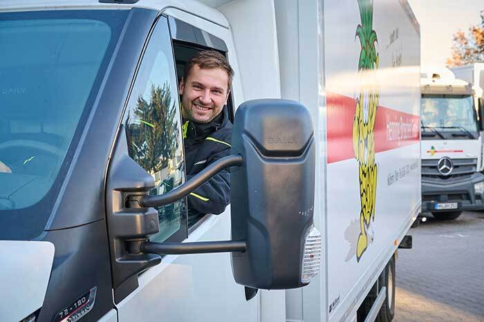 Lächelnder LKW-Fahrer im Broscheit-Foodservice-Lieferfahrzeug vor dem Firmengelände