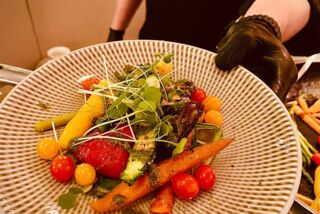 Angerichteter Teller mit buntem Ofengemüse und Microgreens, präsentiert von einem Koch im schwarzen Outfit